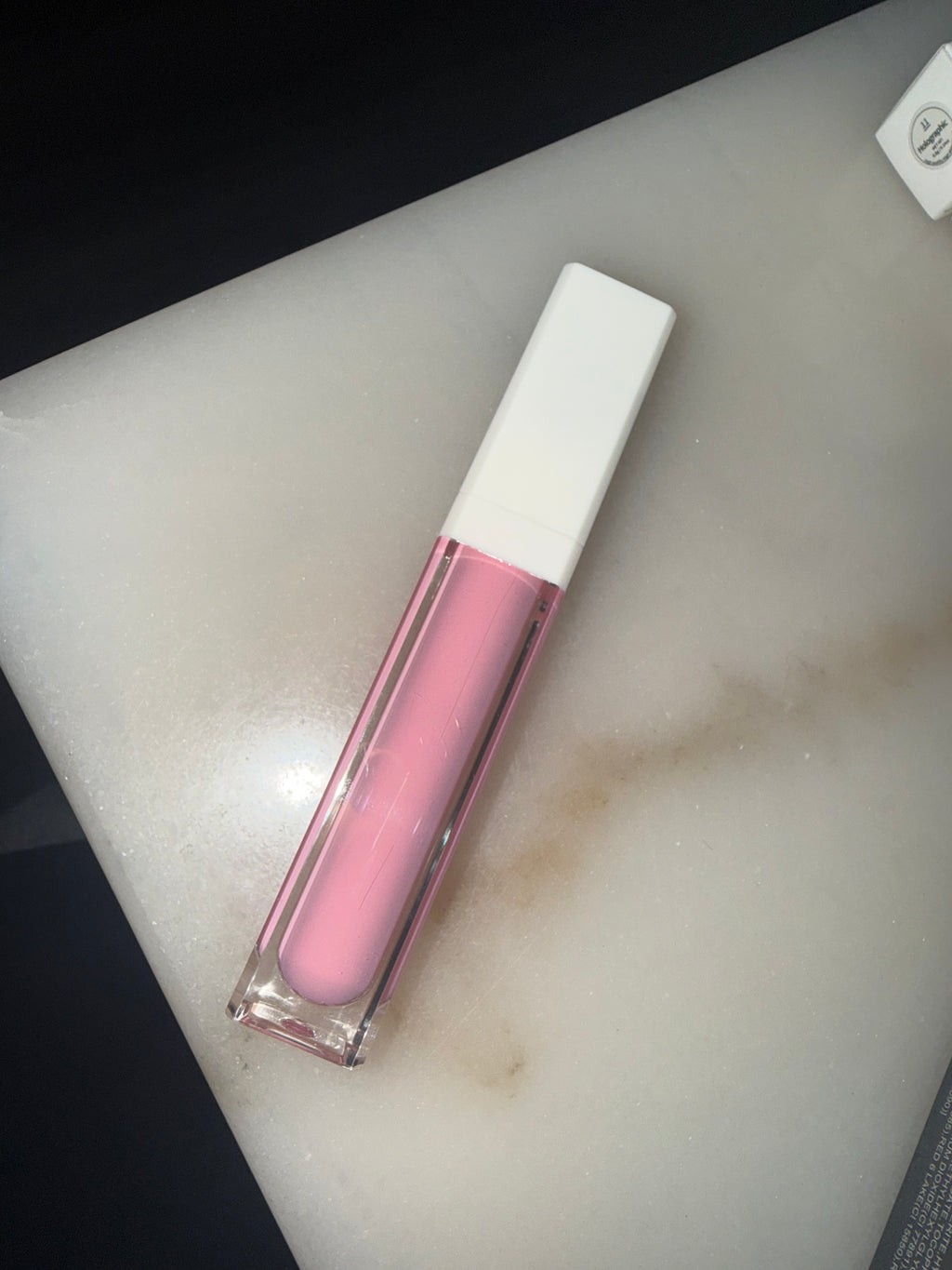 Pink lip gloss with white cap on a light gray surface